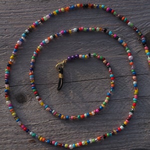 Könnte beinhalten: Eine bunte Perlenkette für Brillen mit goldfarbenen Verschlüssen. Die Kette besteht aus kleinen, mehrfarbigen Perlen und hat eine Länge von etwa 71 cm.