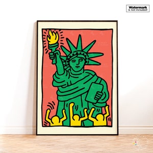 May include: A framed art print featuring a stylized illustration of the Statue of Liberty. The artwork depicts the statue in green with a yellow torch against a red background, with yellow figures at the bottom. The print is in a black frame.