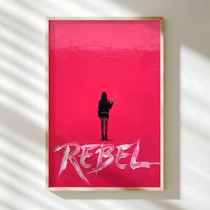 May include: Framed art print featuring a woman standing against a vibrant pink background. The word "REBEL" is written in white brushstrokes across the bottom. The woman is wearing a black jacket and shorts.