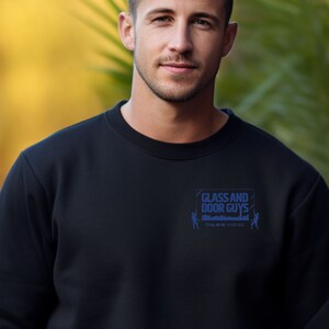 May include: A black crew neck sweatshirt with the text "GLASS AND DOOR GUYS" in blue. The sweatshirt has a small logo on the upper left chest area. The person in the image is wearing the sweatshirt.