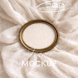 May include: An oval, gold-toned picture frame with a textured edge, positioned on a backdrop of draped, off-white fabric. The frame is empty, ready for a photo or artwork. The words "Frame" and "Mockup" are written on the fabric.