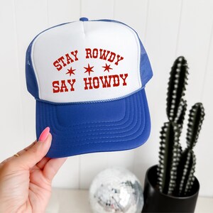 May include: A blue and white trucker hat with the text "Stay Rowdy Say Howdy" in red lettering and three white stars.