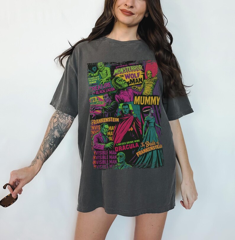 May include: Charcoal grey t-shirt displaying a vibrant collage of vintage monster movie posters. The design showcases images of Frankenstein, Dracula, the Mummy, and the Wolfman, with text including "Monster," "Mummy," and "Frankenstein."