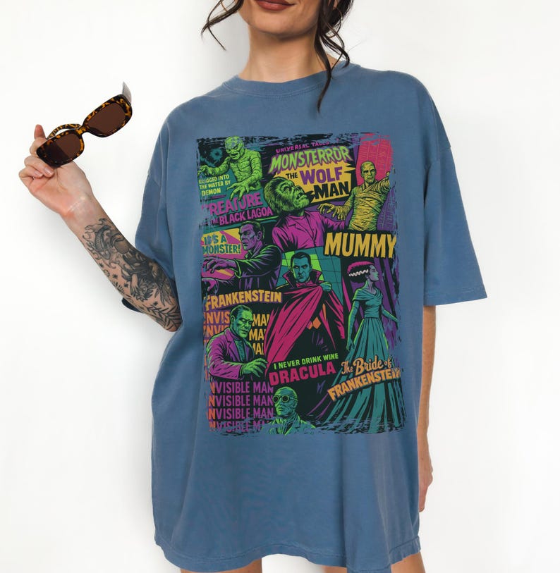 May include: A blue t-shirt with a vibrant graphic of classic Universal Monsters film posters. The design includes images of the Mummy, Frankenstein, Dracula, and the Wolfman. The t-shirt has a relaxed fit.