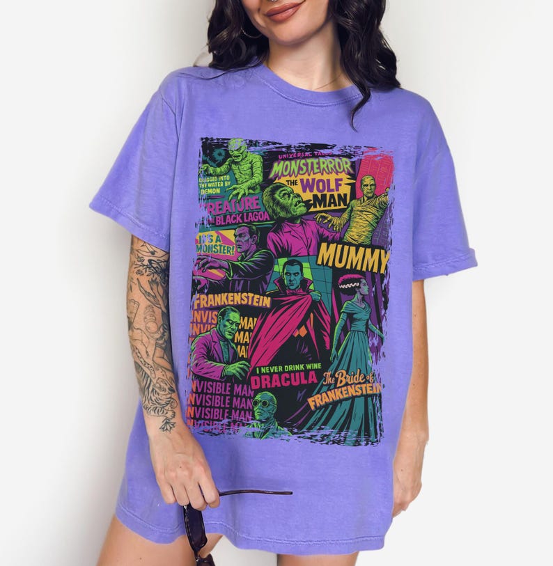 May include: A lilac t-shirt with a vibrant graphic of classic Universal Monsters film posters. The design includes images of Frankenstein, Dracula, The Mummy, and The Wolfman. The t-shirt has a loose fit.