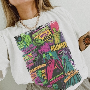 May include: White t-shirt with a vibrant graphic showcasing classic Universal Monsters. The design includes the Creature from the Black Lagoon, the Wolf Man, the Mummy, Dracula, Frankenstein, and the Bride of Frankenstein. Text includes "Monster Terror" and "I never drink wine".