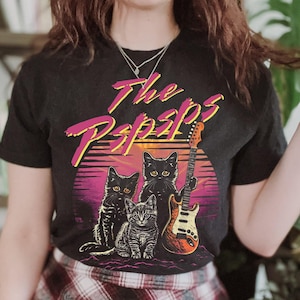May include: Black t-shirt with a graphic of three black cats playing electric guitar. The graphic includes the text "The Pspsps".