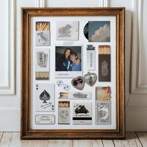 May include: A wooden frame containing a collage of various items including matchboxes with printed graphics, a polaroid-style photo with the text I love you, a heart-shaped locket, two dice, a playing card, and a small rectangular Toronto travel tag.