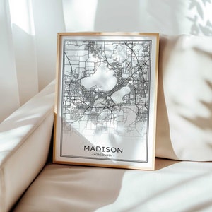 Puede incluir: Una impresión de mapa en blanco y negro de Madison, Wisconsin en un marco dorado. El mapa muestra las calles y los lagos de la ciudad. El texto "MADISON - WISCONSIN -" está impreso debajo del mapa.