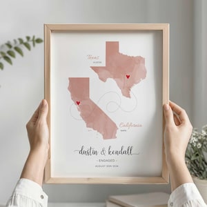 May include: A framed print featuring watercolor-style maps of Texas and California in muted pink tones. A dashed line connects red heart markers on Austin and Napa. The text reads Dustin & Kendall, ENGAGED, and AUGUST 20TH 2024.