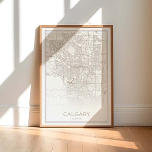 Puede incluir: Un mapa enmarcado de Calgary, Alberta. El mapa está en blanco y negro con un fondo marrón claro. El nombre de la ciudad está impreso en una fuente simple en la parte inferior del mapa.