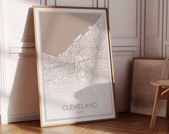 May include: A framed map print of Cleveland, Ohio, with a beige background and white lines depicting the city streets. The frame is a light brown wood.