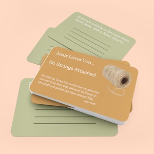 May include: A stack of cards with a light green background and a light brown background. The card on top has the text "Jesus Loves You... No Strings Attached" and a picture of a ball of twine. The text below the picture reads "For God so loved the world that he gave his one and only Son, that whoever believes in him shall not perish but have eternal life. John 3:16".