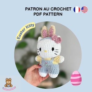 Peut inclure: Un chaton de Pâques en crochet blanc portant une salopette bleue et des oreilles de lapin. Le chaton tient une fleur rose. L'image comprend le texte "Easter Kitty" et "PATRON AU CROCHET PDF PATTERN".