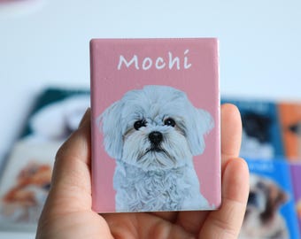 May include: A pink square magnet with a white Maltese dog on it. The dog is looking at the camera and the text "Mochi" is printed above the dog.