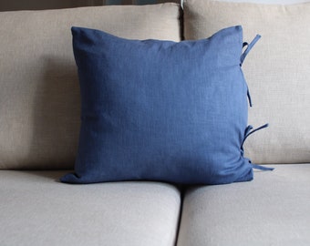 Könnte beinhalten: Ein blaues Leinen-Kissen mit Bändern auf einem hellbeigen Sofa.