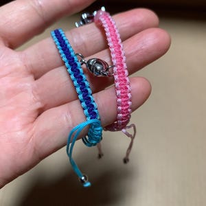 Puede incluir: Dos pulseras de la amistad, una rosa y otra azul y morada, con cierres plateados.