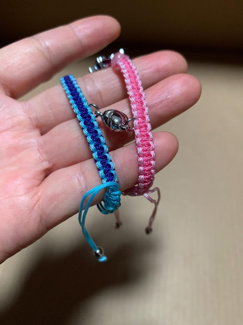 Puede incluir: Dos pulseras de la amistad, una rosa y otra azul y morada, con cierres plateados.