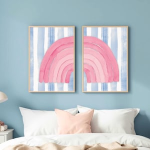 May include: Two rectangular wall art prints in light wood frames, each featuring a vertical blue and white striped background with a partial pink rainbow graphic that completes the arch when placed side by side on a wall.