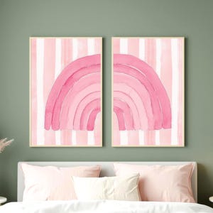 Puede incluir: Dos cuadros rectangulares con un diseño de arcoíris rosa en acuarela dividido. Cada lámina muestra la mitad del arcoíris sobre un fondo de rayas verticales blancas y rosa claro, enmarcado en un marco fino de madera de color claro.