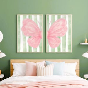 May include: Two rectangular wall art prints displayed side-by-side, each featuring half of a large, soft pink butterfly illustration set against a background of vertical white and sage green stripes, framed in thin, light-coloured wooden frames.