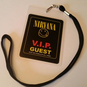 Può includere: Lacci VIP per ospiti di colore nero e giallo con una tessera di plastica nera che presenta la parola "NIRVANA" in lettere gialle, un'emoticon gialla con X rosse per gli occhi e il testo "V.I.P. GUEST" in lettere rosse. Il testo "MUST BE VISIBLE AT ALL TIMES" è stampato in lettere bianche sotto il testo "V.I.P. GUEST".