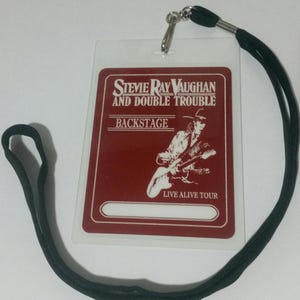 Könnte beinhalten: Ein roter Backstage-Pass mit weißem Rand und dem Text "Stevie Ray Vaughan and Double Trouble" und "Live Alive Tour". In der Mitte des Passes befindet sich eine Schwarzweißillustration eines Mannes, der Gitarre spielt.