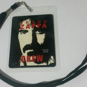 May include: Black and white photo of Frank Zappa on a black lanyard with a clear plastic holder. The text on the holder reads "Frank Zappa Tour 1972 Crew".