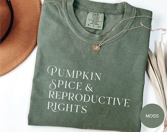 May include: A green t-shirt with the text "Pumpkin Spice & Reproductive Rights" in white lettering. The shirt is a relaxed fit and has a distressed look. The colour of the shirt is called "Moss".