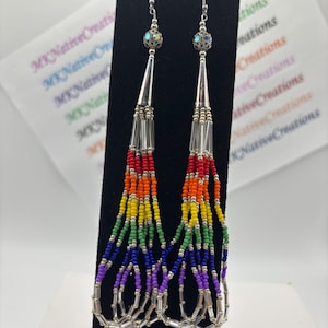 May include: Long dangle earrings featuring a rainbow color gradient of small seed beads in red, orange, yellow, green, blue, and purple. The earrings include silver-toned metal cones, clear glass tube beads, and iridescent spherical accent beads.