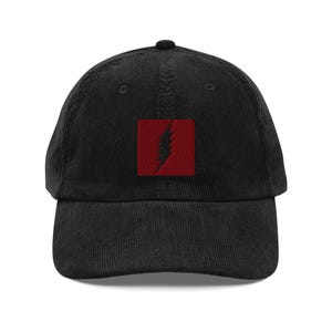 May include: Black corduroy baseball cap with a red square patch featuring a black lightning bolt design. The cap has a curved brim and an adjustable strap for a comfortable fit. A stylish accessory for casual wear.