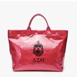 May include: A glossy, red tote bag with a top handle. The bag features a black emblem and the Greek letters ΔΣΘ. The bag is likely made of a shiny, waterproof material.