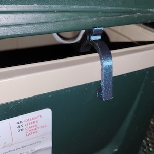 May include: A green cooler with a black latch. The cooler has a label that says "48 Quarts, 45 Liters, 76 Cans, Canettes, Latas".