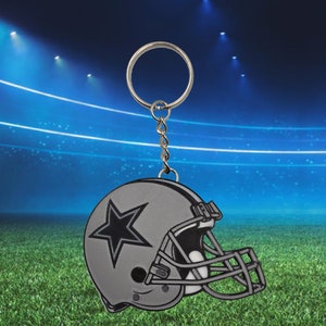 May include: A silver football helmet keychain with a blue star on the side. The keychain is attached to a silver key ring.