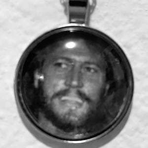 Puede incluir: Un collar de cadena de plata con un colgante redondo que presenta una foto en blanco y negro de la cara de un hombre.