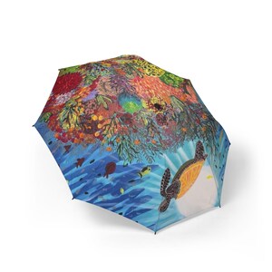May include: A collapsible umbrella featuring a vibrant underwater scene. The canopy displays a colourful coral reef with various textures and shades of red, orange, yellow, and green, alongside a sea turtle swimming in deep blue water.