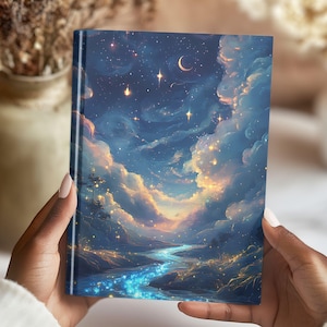 May include: A hardcover journal featuring a celestial landscape with a river, clouds, stars, and a crescent moon. The cover art is a vibrant mix of blues, golds, and whites, creating a dreamy, artistic aesthetic. The journal is held by hands.