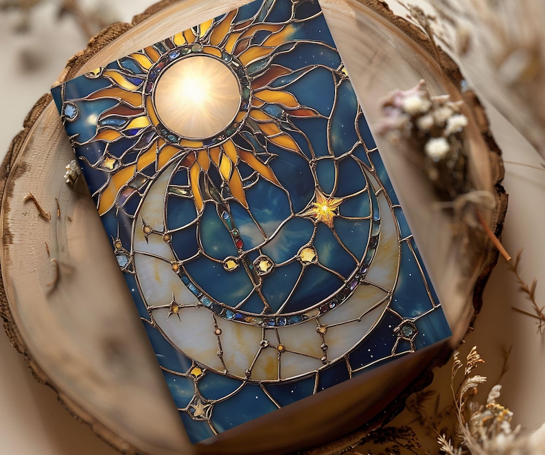 Puede incluir: Una cubierta de cuaderno de vidrio coloreado con un dise&ntilde;o de sol y luna. El sol es amarillo y naranja con un centro brillante. La luna es blanca con un contorno dorado. El fondo es azul con estrellas doradas.