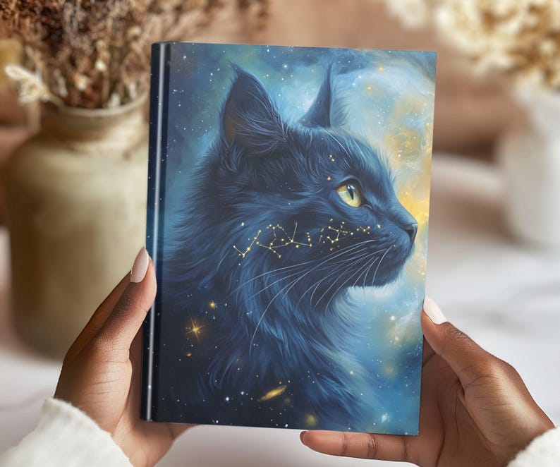 May include: A hardcover journal featuring a celestial cat design. The cover art depicts a black cat's profile against a starry, blue and yellow background. The cat's fur is detailed, and constellations are subtly placed on its face.