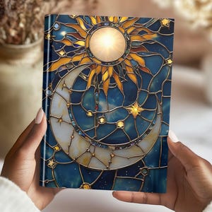 Puede incluir: Una cubierta de cuaderno de vidrio coloreado con un dise&ntilde;o de sol y luna. El sol es amarillo y dorado con un centro blanco. La luna es blanca con un contorno dorado. El fondo es azul con estrellas doradas.