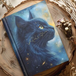 May include: A hardcover journal featuring a black cat with a celestial design. The cat's fur is a deep blue, and golden constellations adorn its face. The background is a blend of blue and yellow, creating a starry night sky effect.