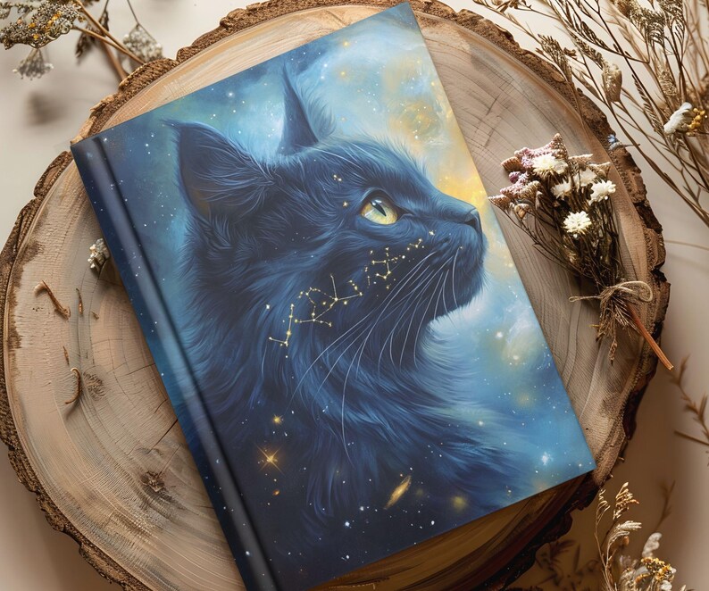 May include: A hardcover journal featuring a black cat with a celestial design. The cat's fur is a deep blue, and golden constellations adorn its face. The background is a blend of blue and yellow, creating a starry night sky effect.