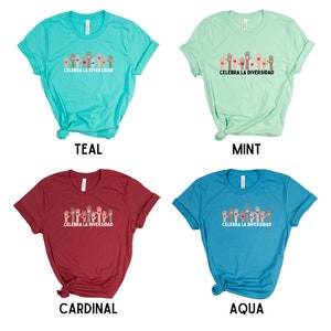 May include: Four t-shirts in teal, mint, cardinal, and aqua. Each shirt features a graphic of raised hands in various skin tones with hearts, and the text "CELEBRA LA DIVERSIDAD" in white. The shirts are short-sleeved.