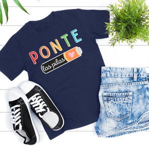 May include: A navy blue t-shirt with the text "PONTE las pilas" in rainbow colors and a battery with a heart on it.