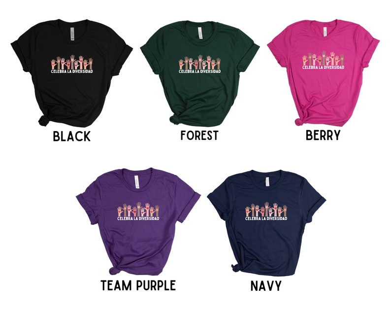 May include: A collection of t-shirts in various colors: black, forest green, berry pink, team purple, and navy blue. Each shirt features a graphic of raised hands in different skin tones above the text "CELEBRA LA DIVERSIDAD".
