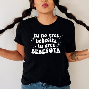 May include: Black t-shirt with white text that reads "tu no eres bebecita tu eres bebesota" with stars around the text.