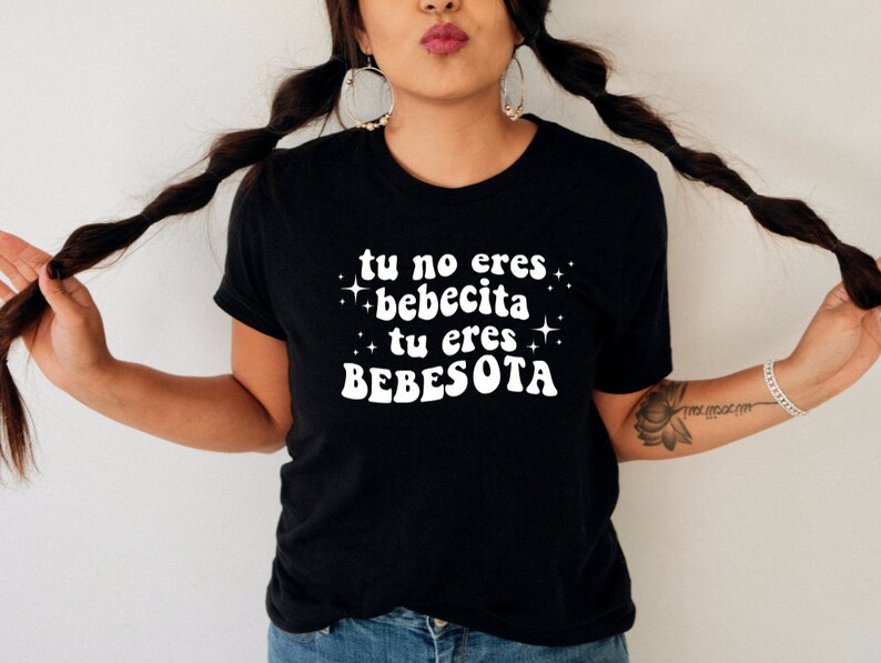 May include: Black t-shirt with white text that reads "tu no eres bebecita tu eres bebesota" with stars around the text.