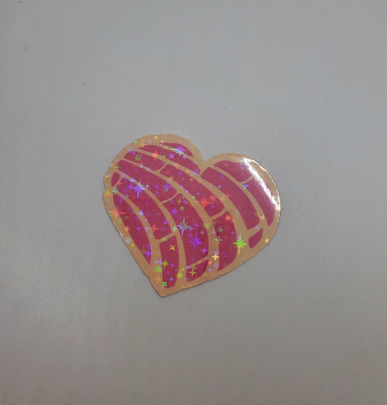 Pu&ograve; includere: Un adesivo a forma di cuore con un design rosa e oro. Il design &egrave; un pane dolce messicano tradizionale chiamato concha, con un motivo a stelle.