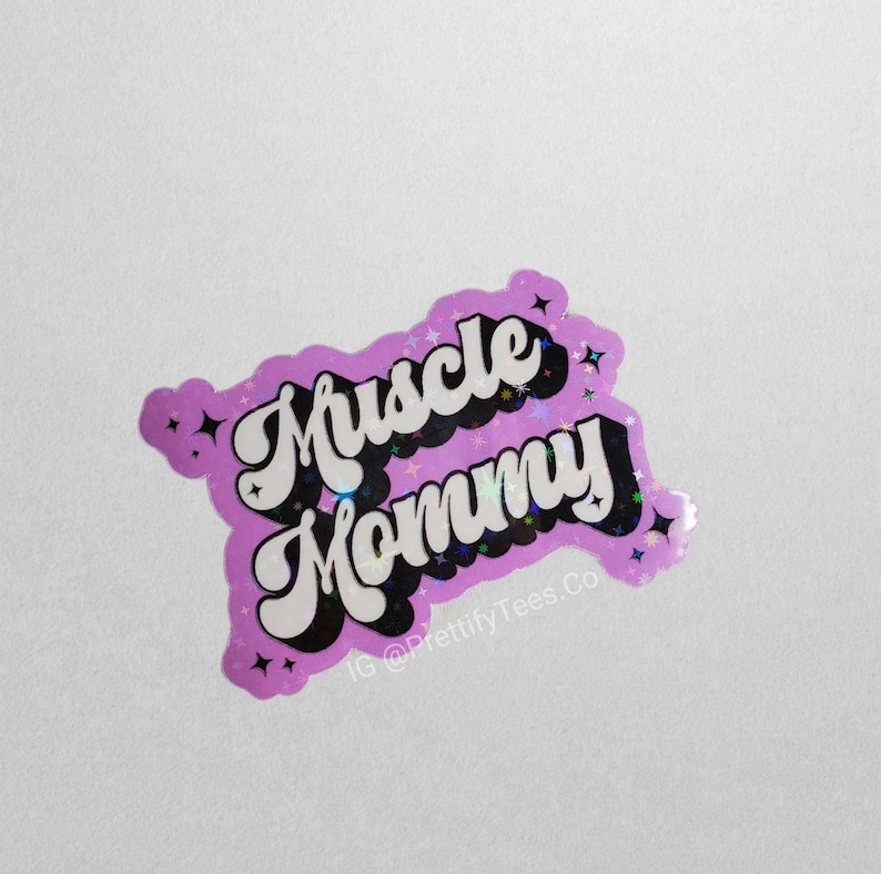 K&ouml;nnte beinhalten: Ein pinkfarbener holografischer Aufkleber mit dem Text "Muscle Mommy" in einer Retro-Schriftart. Der Aufkleber hat eine glitzernde Oberfl&auml;che und enth&auml;lt den Instagram-Handle "@PrettifyTees.Co".