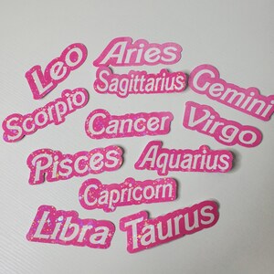 May include: Pink and white glitter stickers with the names of the 12 zodiac signs: Aries, Taurus, Gemini, Cancer, Leo, Virgo, Libra, Scorpio, Sagittarius, Capricorn, Aquarius, and Pisces.